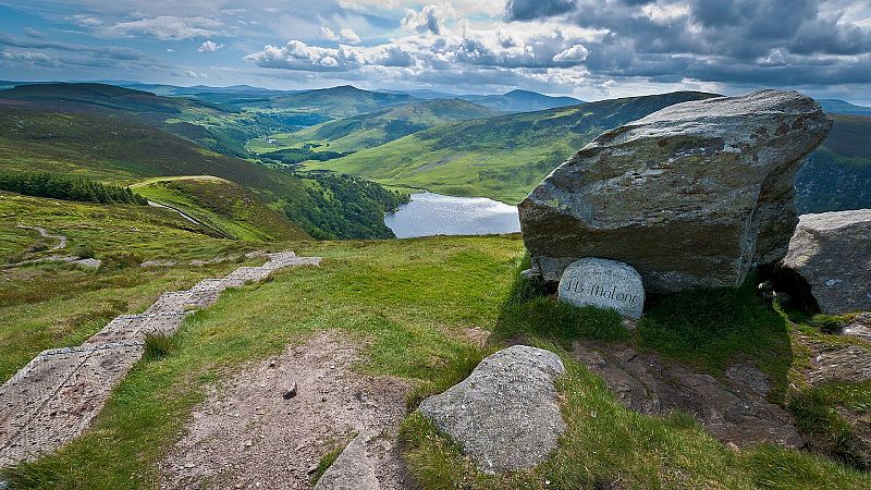 Paisaje monta�oso en Irlanda con valle, un lago y un monumento conmemorativo de roca con el nombre 'J.B. Malone' junto a un sendero.