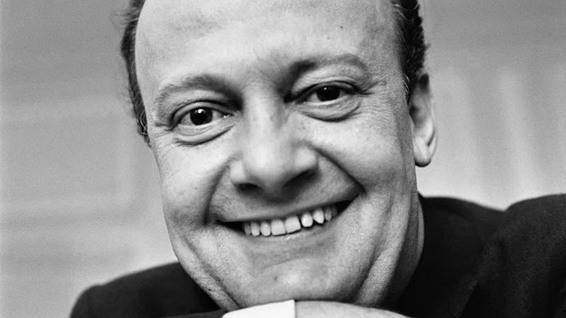Primer plano en blanco y negro del bar�tono Tito Gobbi sonriendo alegremente a la c�mara con la barbilla apoyada en la mano.