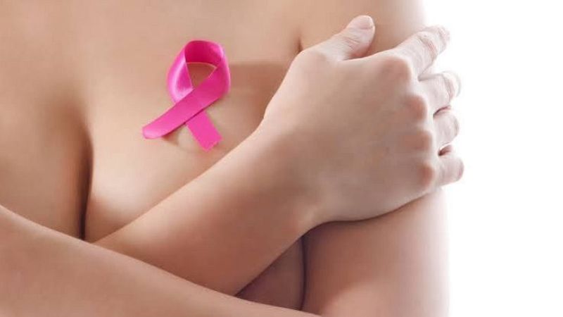 Primer plano de una mujer con los brazos cruzados sobre el pecho y un lazo rosa de concienciaci�n contra el c�ncer de mama sobre su piel.