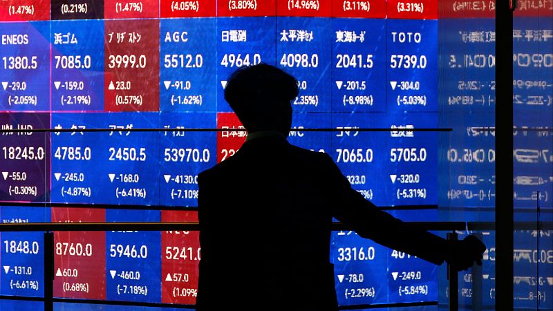 Silueta de espaldas de una persona contemplando una enorme pantalla luminosa con datos financieros de la Bolsa de Tokio.