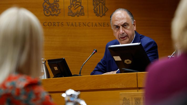 Hombre con traje azul interviene ante una mesa con micrófono en una sala con paneles de madera y el texto Corts Valencianes de fondo.