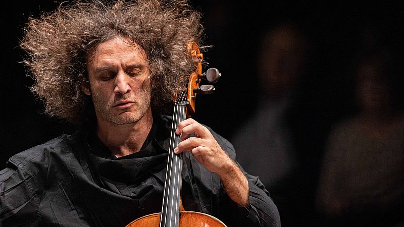Plano medio de Nicolas Altstaedt tocando el violonchelo con profunda concentraci�n, destacando su melena rizada y una iluminaci�n dram�tica sobre fondo oscuro.