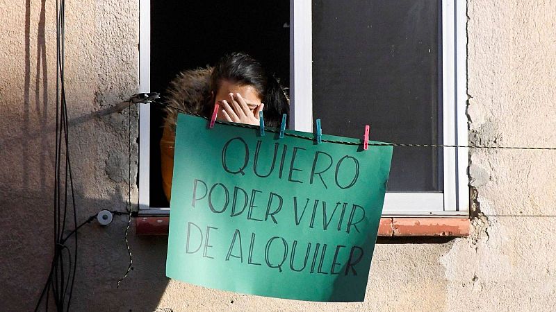 Persona asomada a una ventana tras una pancarta verde con el mensaje «QUIERO PODER VIVIR DE ALQUILER» sujeta a un tendedero.