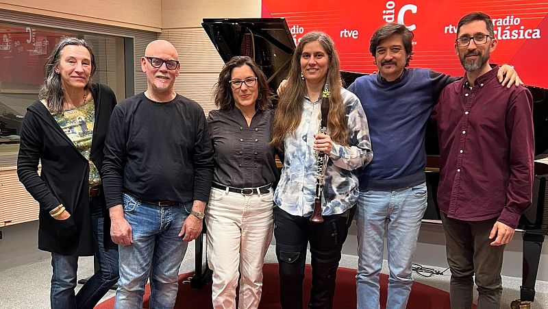 Grupo de seis personas posando sonrientes en un estudio de grabaci�n con pared roja de fondo, una de ellas sosteniendo un clarinete.