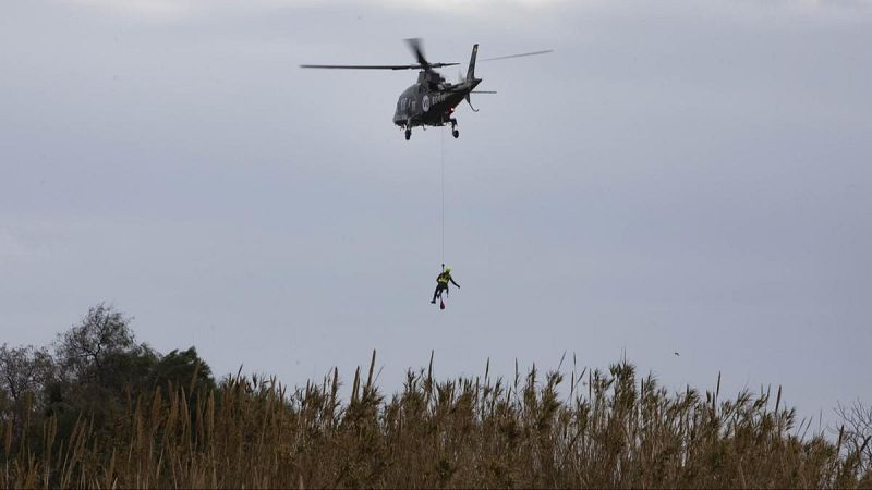 Helicóptero de emergencias realizando una maniobra de rescate con un rescatista descendiendo en un cañaveral.