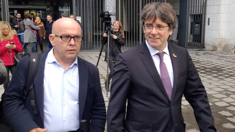 Carles Puigdemont y su abogado Gonzalo Boye caminan juntos en exteriores, acompa�ados por la presencia de medios de comunicaci�n y prensa.