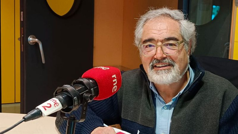 Eduard Sala sonr�e ante la c�mara en un estudio de radio, sentado junto a un micr�fono con el logotipo de rne.