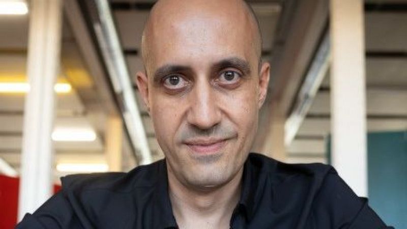 Primer plano del compositor Luis Tabuenca, calvo y con camisa negra, mirando a c�mara en un espacio interior de estilo industrial.