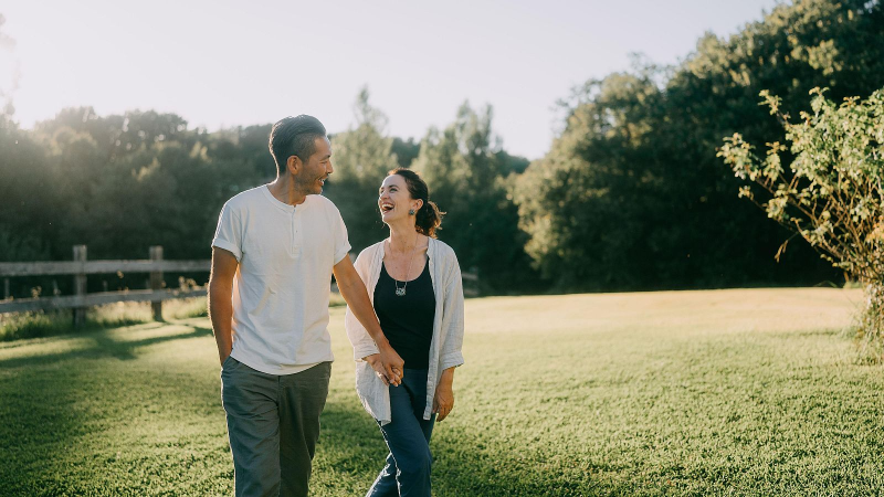 Pareja caminando de la mano y sonriendo alegremente en una pradera verde durante el atardecer, con una c�lida luz natural.