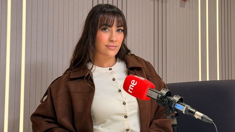 Miriam Saint Germain sonr�e en un estudio de radio ante un micr�fono con el logotipo de RNE y un fondo de paneles ac�sticos.