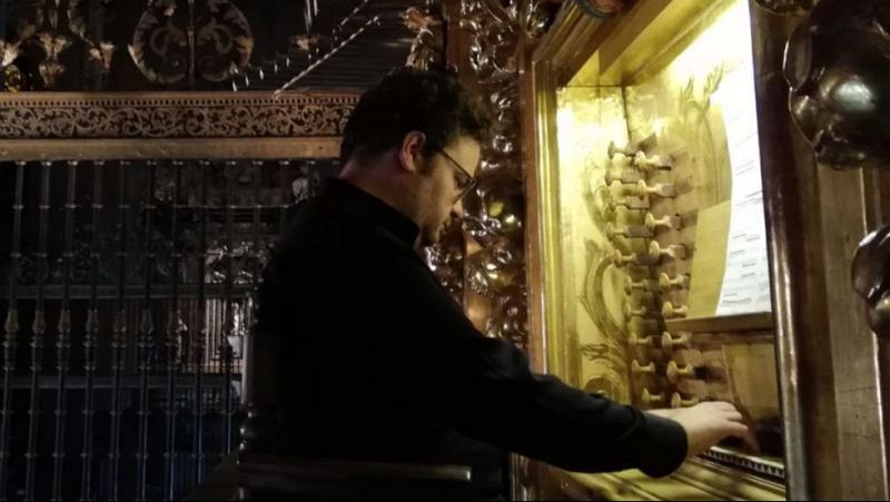 Un organista con gafas y camisa negra toca un hist�rico �rgano barroco de madera dorada con partituras iluminadas.