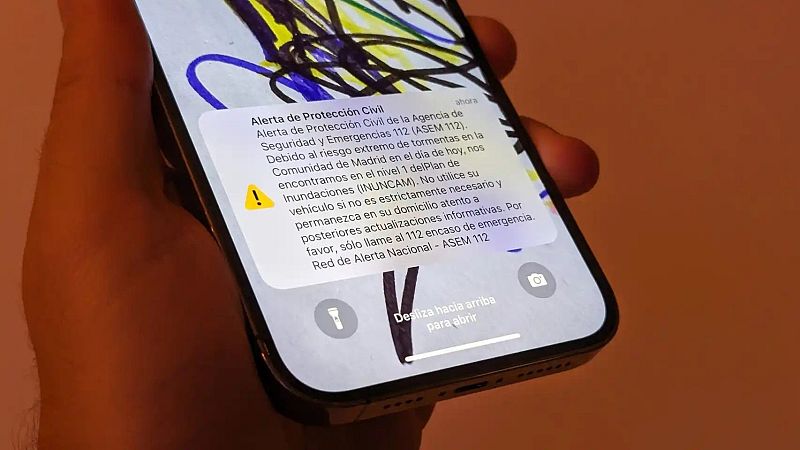 Persona sosteniendo un smartphone con una notificación de alerta de Protección Civil por riesgo de tormentas en su pantalla de bloqueo.