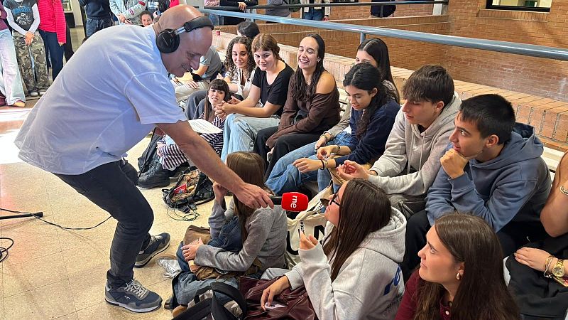 Un reportero con micr�fono de RNE entrevista a estudiantes sentados en las gradas de un centro educativo.