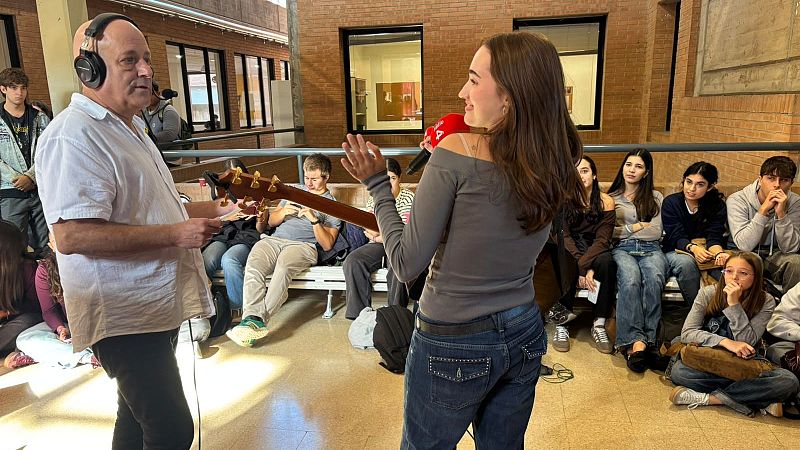 La cantante Helga sostiene un micr�fono con capuch�n rojo durante una entrevista en un pasillo universitario ante la atenta mirada de varios estudiantes.