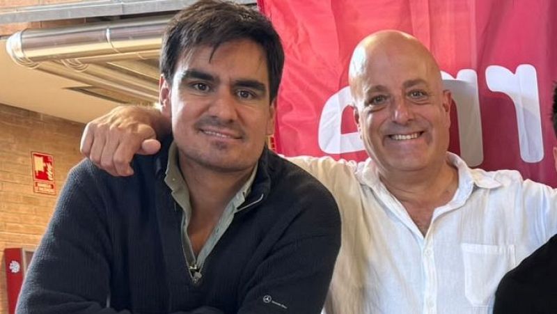 Dos hombres sonr�en amistosamente en un estudio de radio, con una pancarta corporativa roja y una pared de ladrillo al fondo.