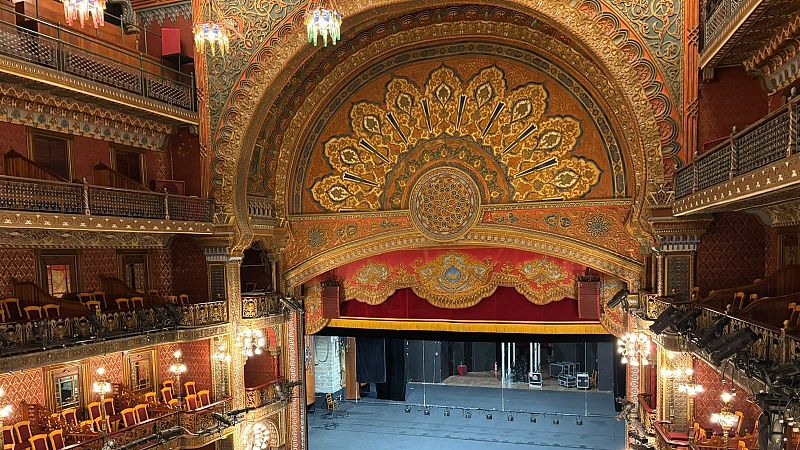 Vista elevada del interior del Teatro Juárez con su monumental arco de proscenio decorado, palcos con barandillas de bronce y butacas rojas.