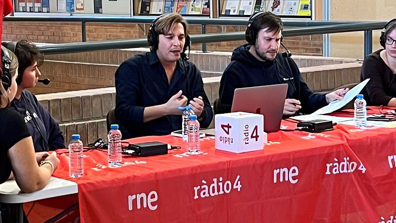 Emisi�n de radio en directo desde una instituci�n con una mesa cubierta de mantel rojo, material t�cnico y equipo con auriculares.