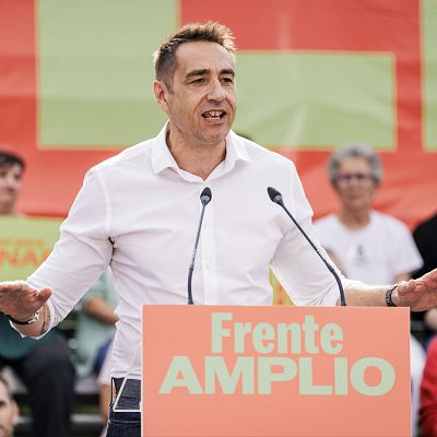 Plano medio de Emilio Delgado Orgaz hablando tras un atril con la inscripción «Frente AMPLIO», vistiendo camisa blanca y gesticulando.