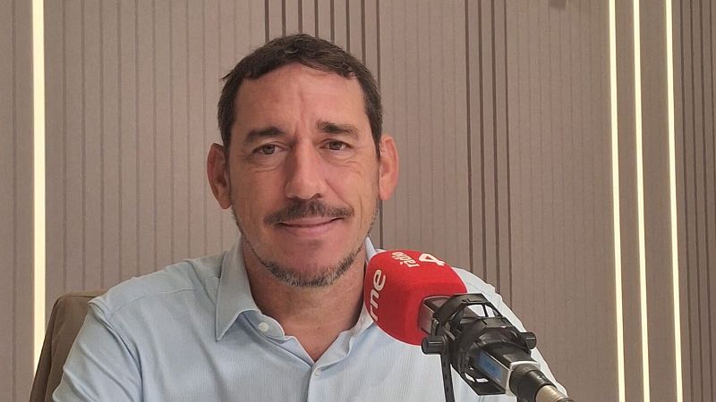 Hombre de mediana edad sonr�e en un estudio de radio ante un micr�fono con funda roja y fondo de madera.