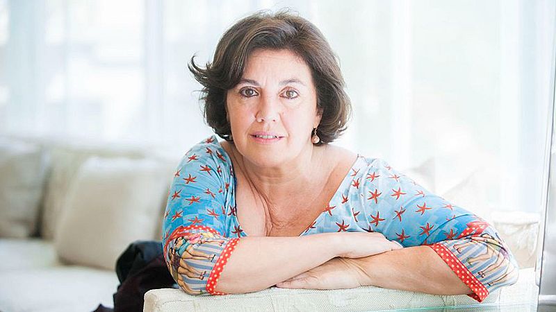 Plano medio de la periodista Conxita Casanovas, con blusa azul estampada y expresi�n serena, apoyada en un sill�n en una estancia luminosa.