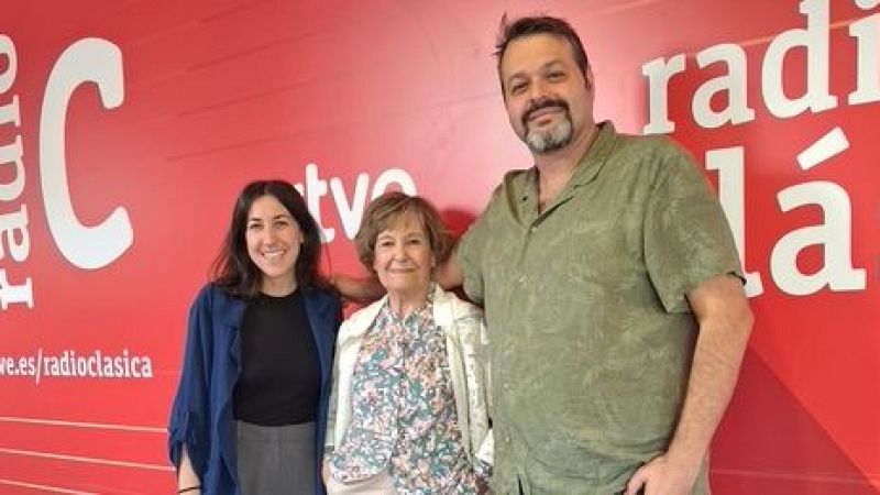 Tres personas posan sonrientes ante una pared corporativa roja de Radio Cl�sica, incluyendo a la actriz Luz Olier en el centro flanqueada por Clara S�nchez y Mart�n Llade.