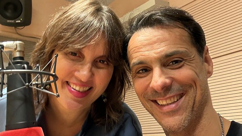 Selfie de la periodista Olga Baeza y el bailarín Igor Yebra sonriendo juntos en el interior de un estudio de radio con paneles de madera.