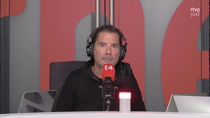 Presentador con sudadera negra y auriculares en un estudio de radio, con un micr�fono de espuma roja y el logotipo de rtve play visible.