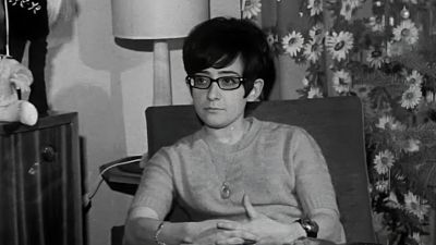Fotograf�a en blanco y negro de la joven m�sica Maryn� Callejo sentada en una butaca, con gafas oscuras, jersey de punto y una expresi�n serena en un entorno dom�stico.