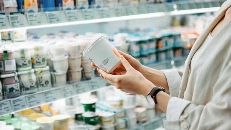 Una persona sostiene una tarrina de pl�stico en el pasillo de refrigerados de un supermercado para leer su etiqueta.