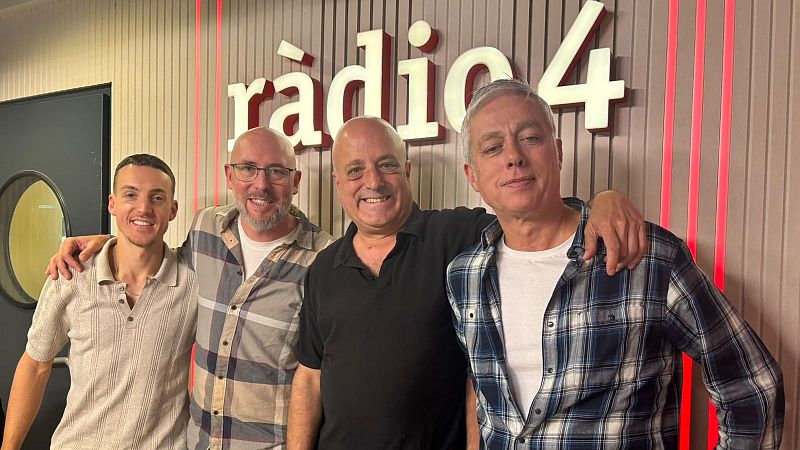 Cuatro hombres sonrientes posan abrazados en un estudio de radio con paneles acústicos iluminados por luces LED rojas y el logotipo luminoso de ràdio 4.