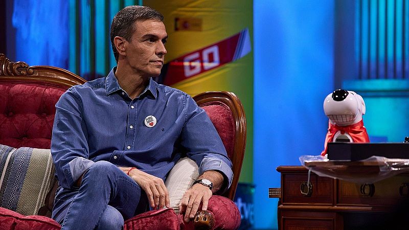 Pedro S�nchez sentado en un sill�n rojo en un plat� de televisi�n, con camisa vaquera, chapa identificativa y un mu�eco decorativo al lado.