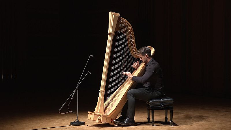 El arpista Xavier de Maistre toca un arpa cl�sica de madera en un escenario oscuro, iluminado por un foco c�lido que resalta al m�sico y al instrumento.