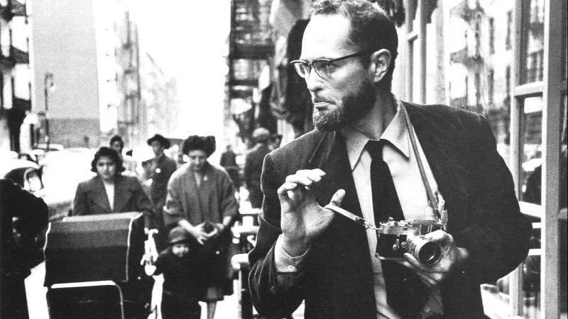 Fotograf�a en blanco y negro del fotoperiodista W. Eugene Smith con c�mara en mano caminando por una calle urbana de mediados del siglo XX.