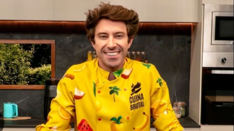 El chef Roberto Bosquet sonr�e en una cocina moderna vistiendo una chaquetilla amarilla con dibujos de frutas frente a una pared de piedra oscura.