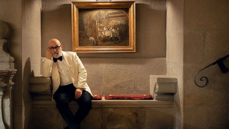 El actor Javier C�mara posa elegante con esmoquin y barba gris�cea sentado en un banco de piedra bajo un cuadro cl�sico.