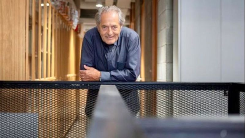 Plano medio de Paco Poch con camisa azul oscura, apoyado en una barandilla met�lica en un pasillo moderno.