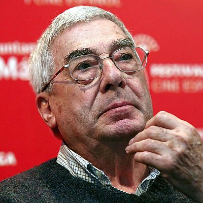 Primer plano del guionista Rafael Azcona con gesto pensativo sobre fondo rojo corporativo.