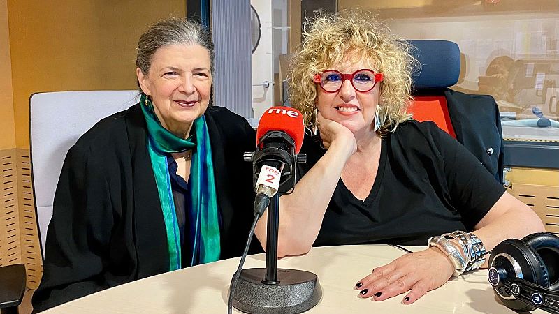 Dos mujeres sonrientes en un estudio de radio ante una mesa de locuci�n con un micr�fono de RNE, con Mary Ann Newman a la izquierda y la periodista Gema Soriano a la derecha.