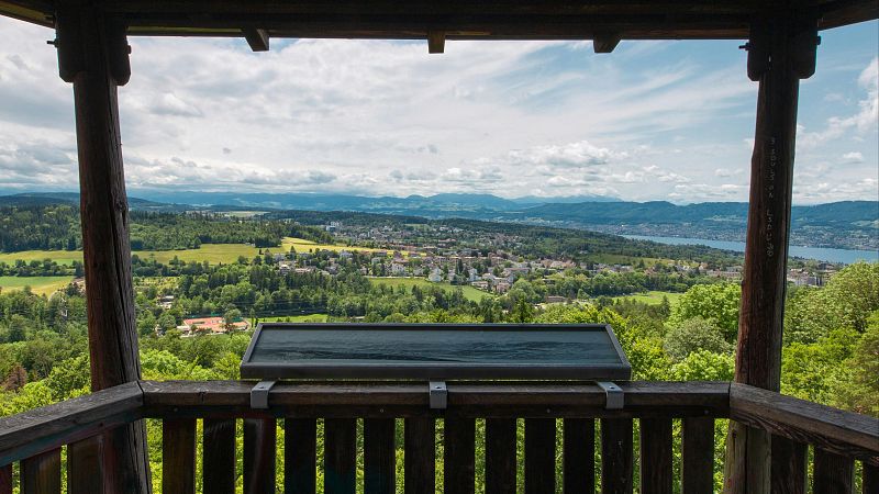 Vista panor�mica de un valle con bosques, una localidad y un lago desde un mirador de madera con panel topogr�fico.