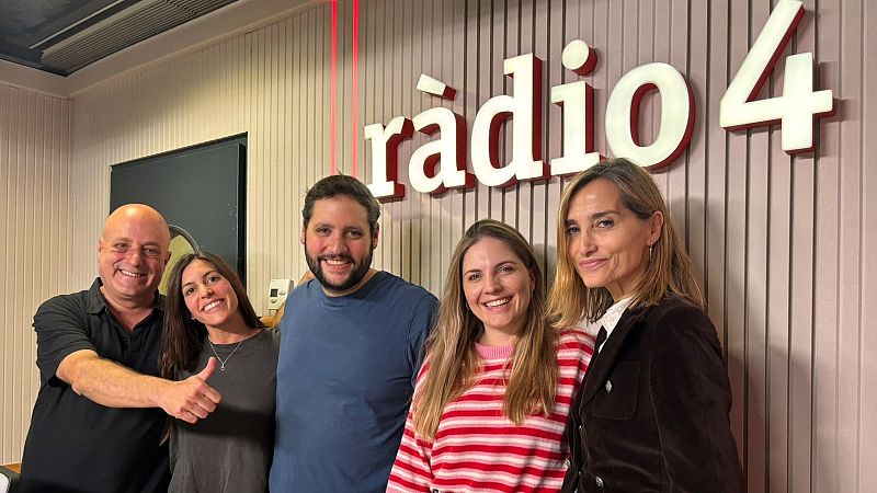 Cinco personas posan sonrientes en un estudio de radio frente a una pared de listones de madera con el logotipo de R�dio 4, transmitiendo una atm�sfera de compa�erismo.