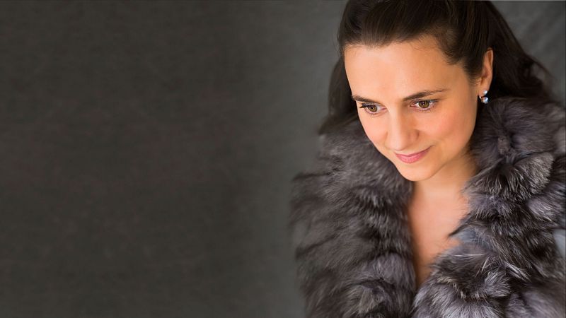 Retrato de estudio de la soprano Nuria Rial con una estola de pelo gris y plateado, expresando serenidad con la mirada baja.