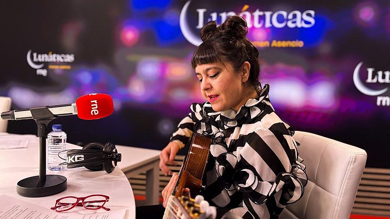 La artista Maui de Utrera toca la guitarra española en un estudio de radio, luciendo una blusa de rayas y dos moños altos.