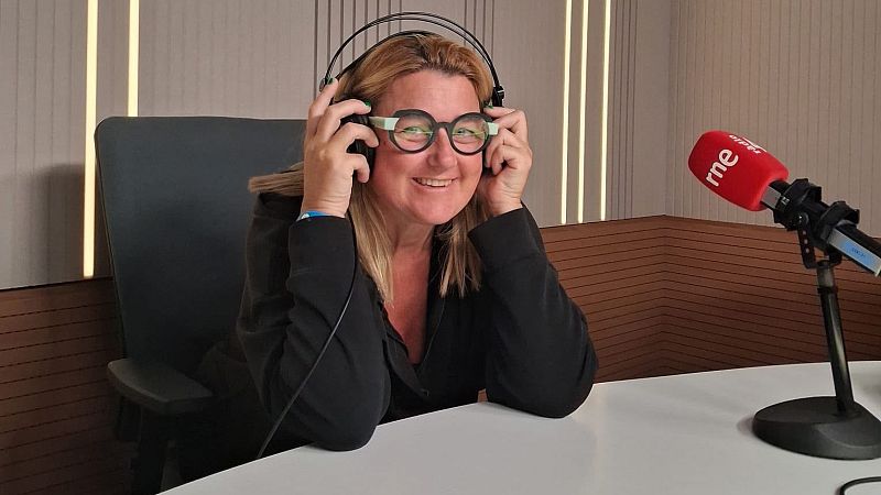 Imma Sust sonr�e en un estudio de radio mientras se ajusta unos auriculares y posa junto a un micr�fono con espuma roja y el logotipo de RNE.