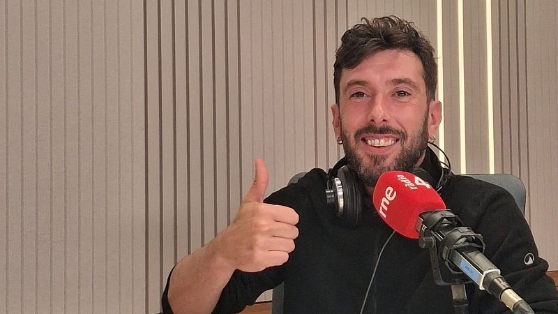 Marc Llibre sonr�e en un estudio de radio con paneles ac�sticos, haciendo el gesto de aprobaci�n y con un micr�fono con capuch�n rojo en primer plano.