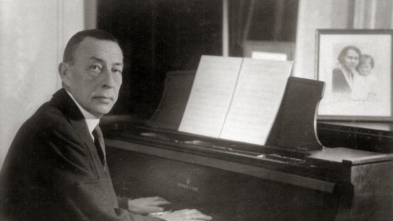 Fotograf�a en blanco y negro del compositor Sergu�i Rajm�ninov con traje formal sentado ante un piano de cola.