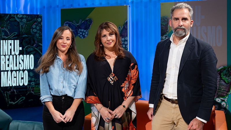 Tres personas posan en un plat� con paneles verdes e iluminaci�n azul, acompa�adas por un t�tem con el texto 'INFLU-REALISMO M�GICO'.