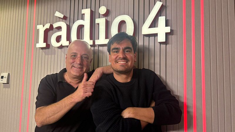 Dos hombres sonrientes posan en los estudios de R�dio 4 ante una pared con el logotipo corporativo iluminado.