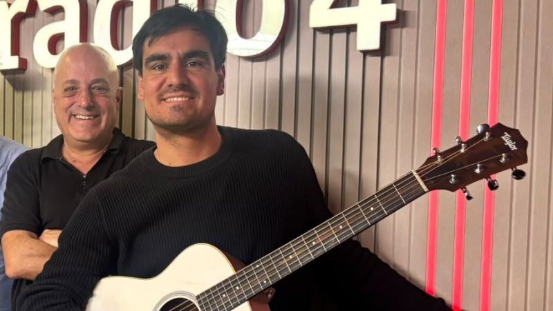 El cantautor Lo Pau de Ponts sonr�e en un estudio de radio sosteniendo una guitarra, acompa�ado por el periodista Carles Mesa bajo el logotipo de R�dio 4.