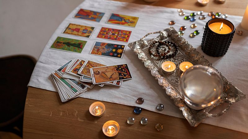 Cartas de tarot, velas y objetos esot�ricos dispuestos sobre una mesa de madera con mantel blanco, creando una atm�sfera m�stica.