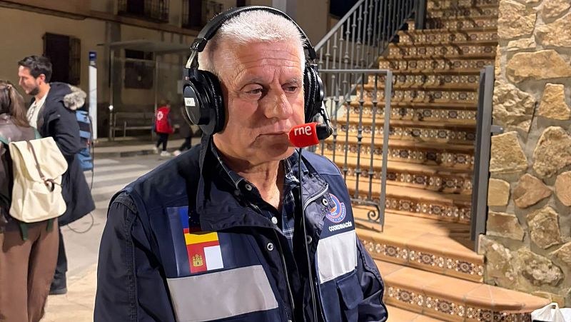 El periodista Josep Cuní, con chaleco de emergencias y auriculares, transmite de noche en un puesto de ayuda humanitaria en Castilla-La Mancha.